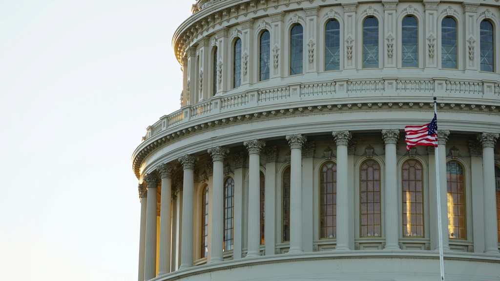 Close-up of the US Capitol building, showcasing its stone columns and an American flag waving.
