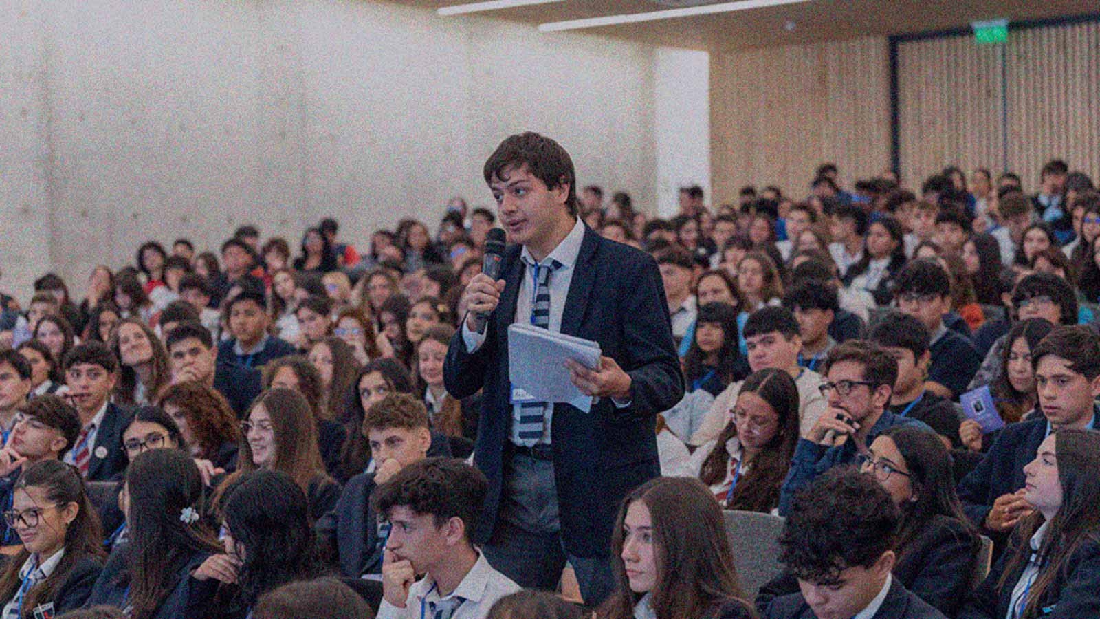 Foto de un joven que habla con un micrófono en un evento con numerosos jóvenes en la columna de opinión Una juventud que participa distinto de IdeaPaís.