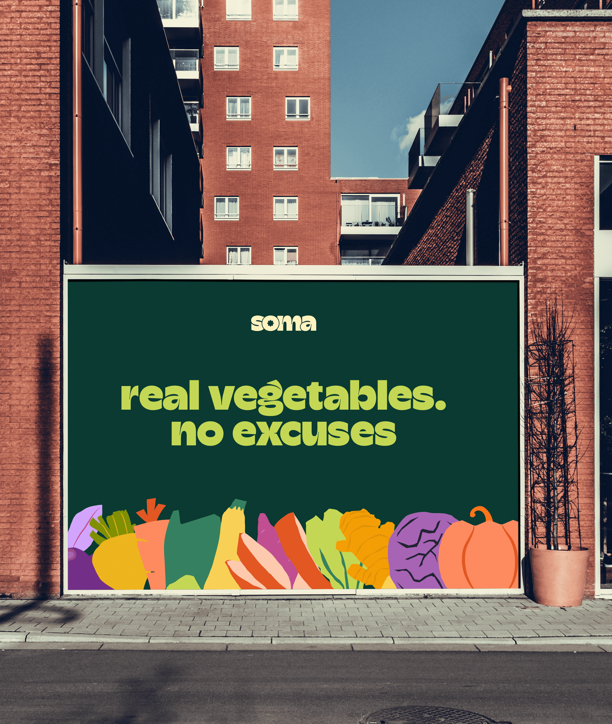 A horizontal street-level billboard mockup for SOMA positioned against a modern red-brick building. The creative features the brand logo and the tagline "real vegetables. no excuses." in a thick, lime-green sans-serif font. A row of colorful, stylized vegetable icons lines the bottom of the dark green canvas.