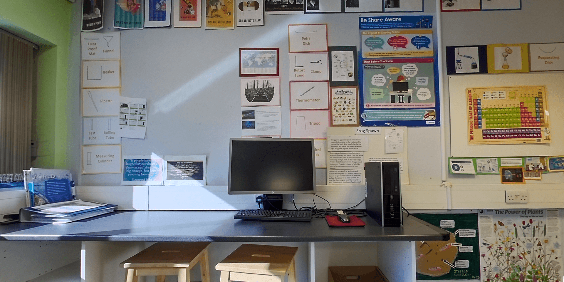 Computer on a desk with seats around it, surrounded by detailed information sheets on a wall, indicative of a learning and collaborative work environment