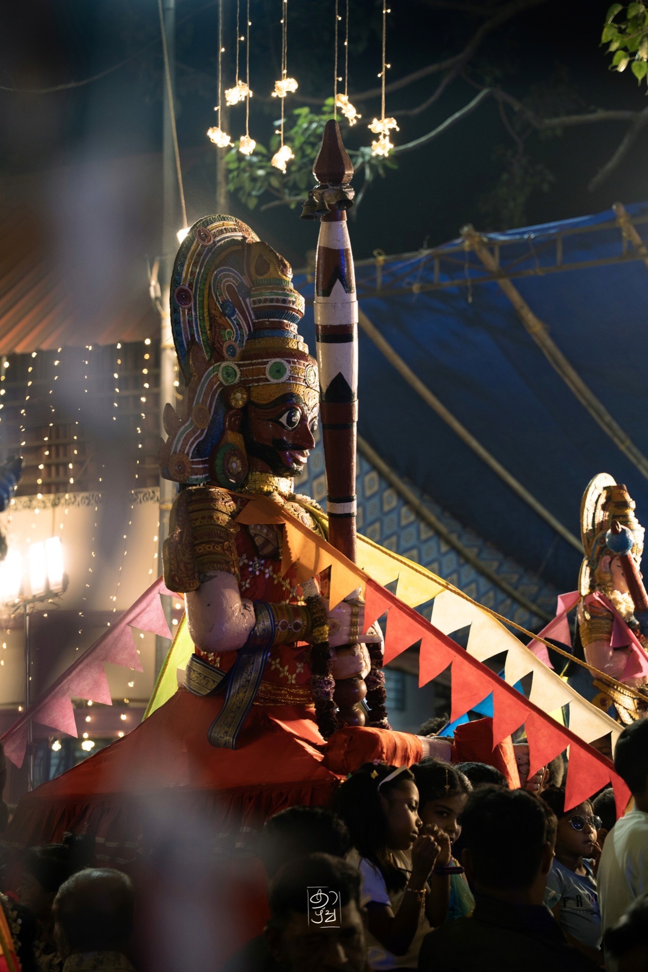 A figure beside the hanging lamps and the festival tent