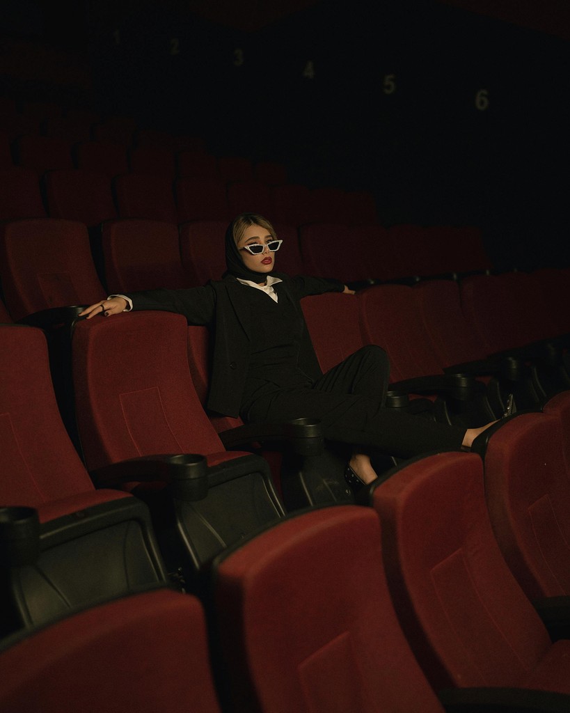 Close-up portrait of a person wearing a gray insulated hooded jacket with the hood up, showing their face framed by the hood against a light background.