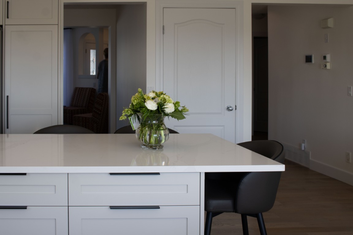 Image of KHD Homes kitchen island with vase of flowers, white countertop, and black chairs, modern interior design.