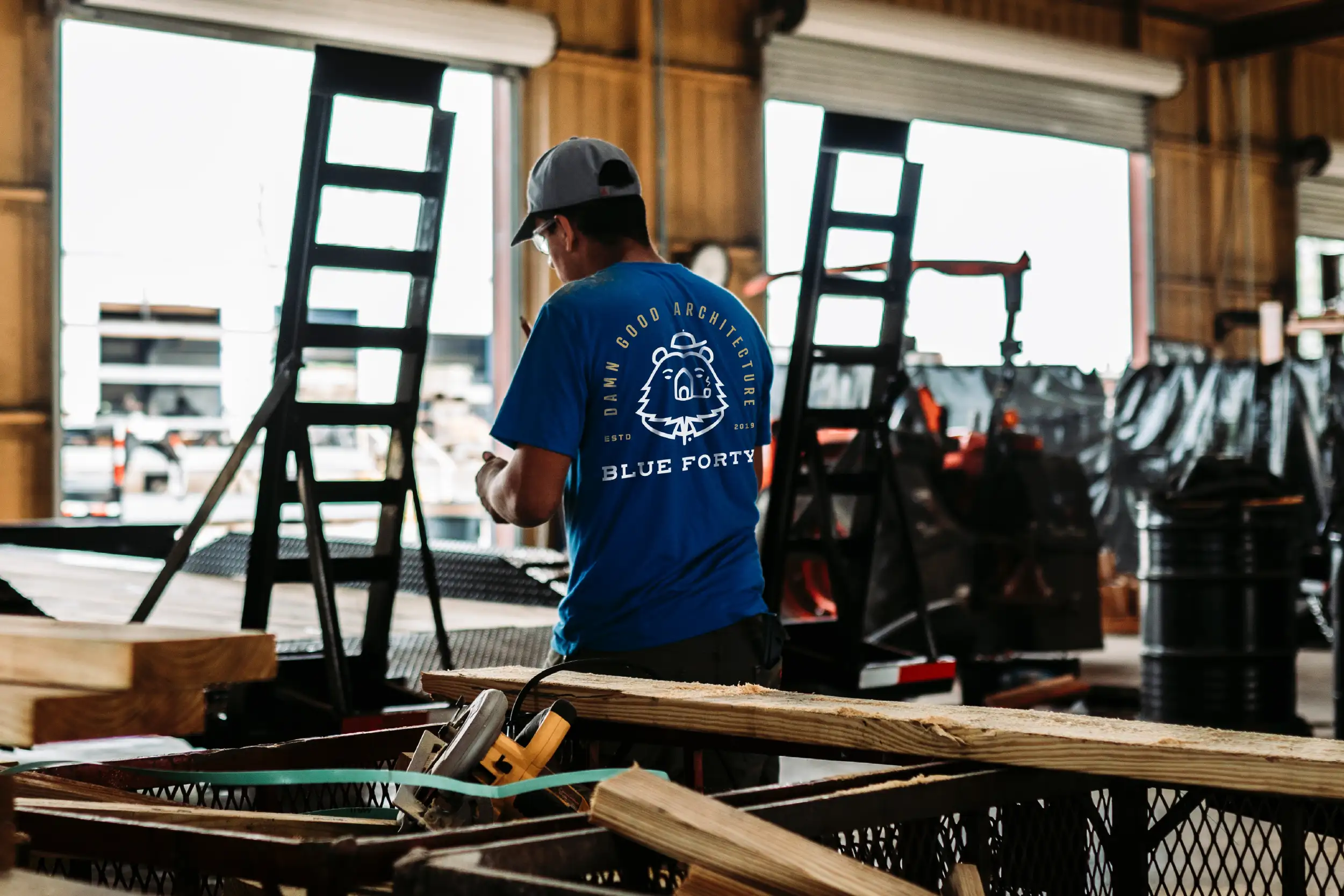 Person wearing a Blue Forty bear badge graphic T-shirt working in a workshop surrounded by wood and tools.