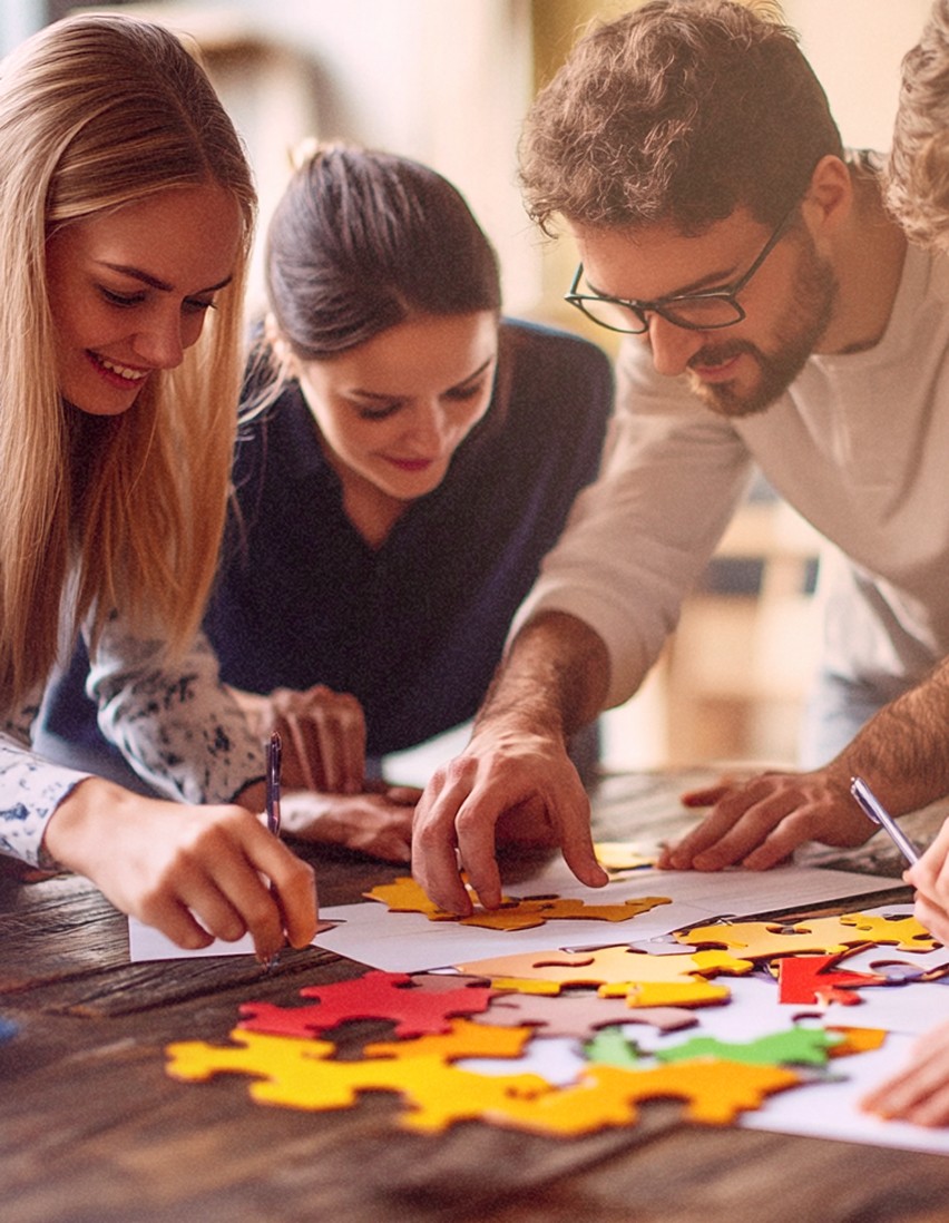 Des personnes travaillant ensemble pour assembler des pièces de puzzle colorées sur une table en bois.