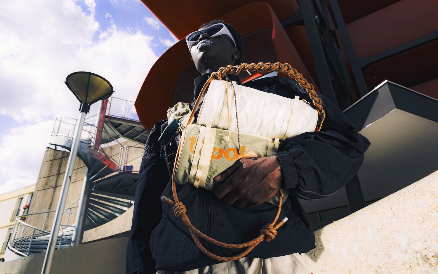 Vue en contre-plongée, une homme porte deux sacoches, marque Topologie apparente
