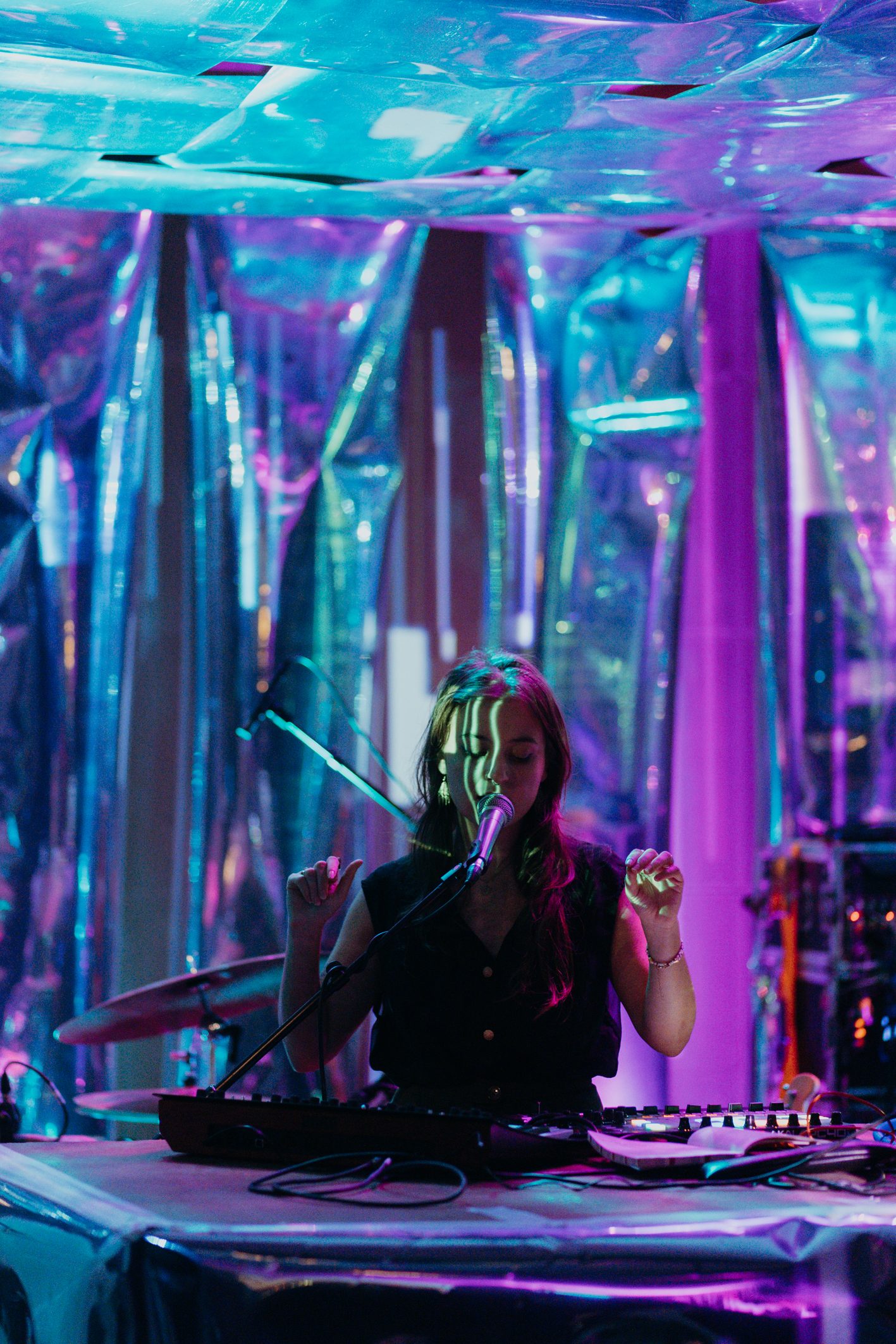 A performer with a headset at a desk inside a cube of iridescent foil