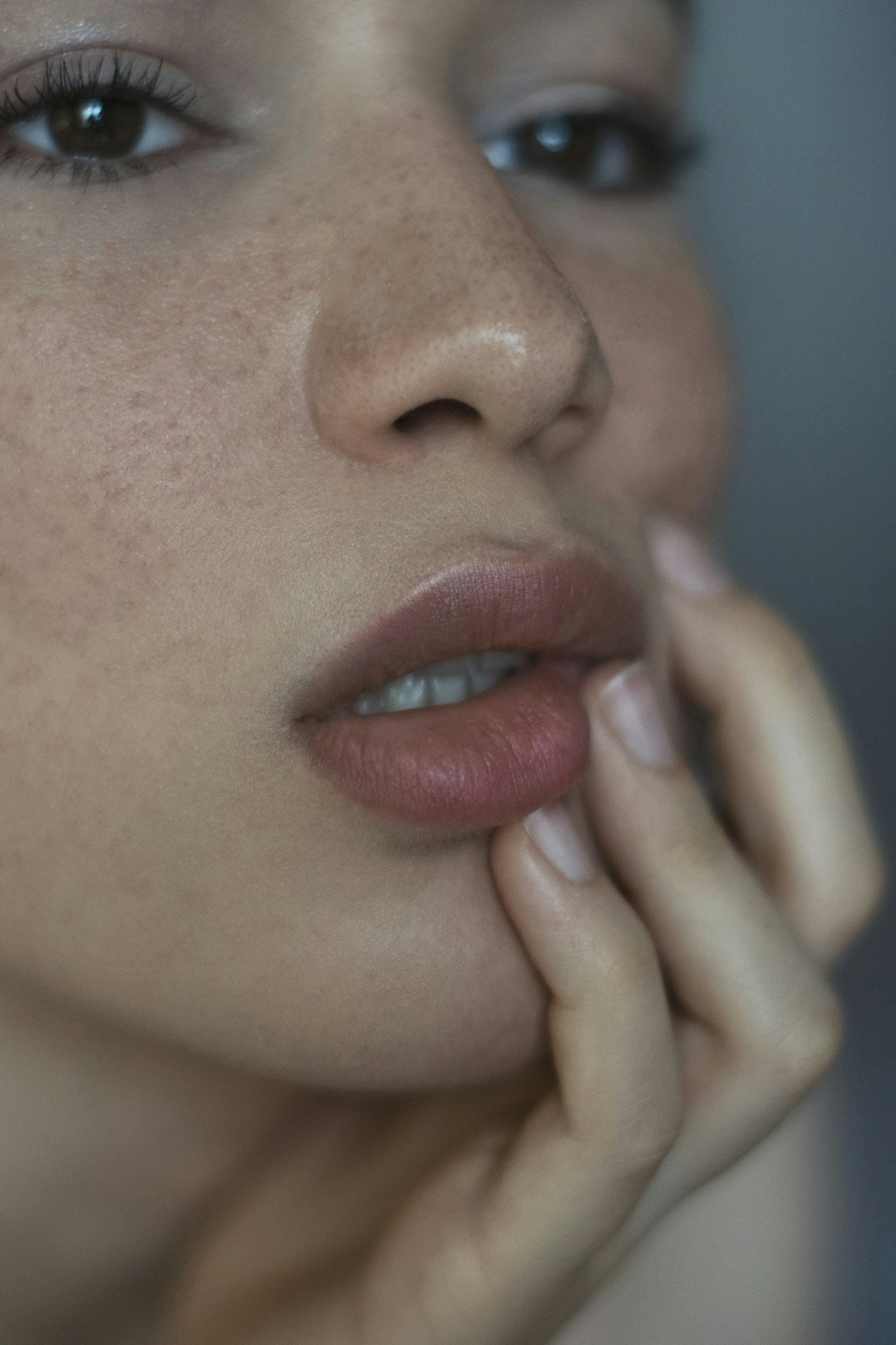 Close portrait of a woman with freckled skin resting a hand near her mouth