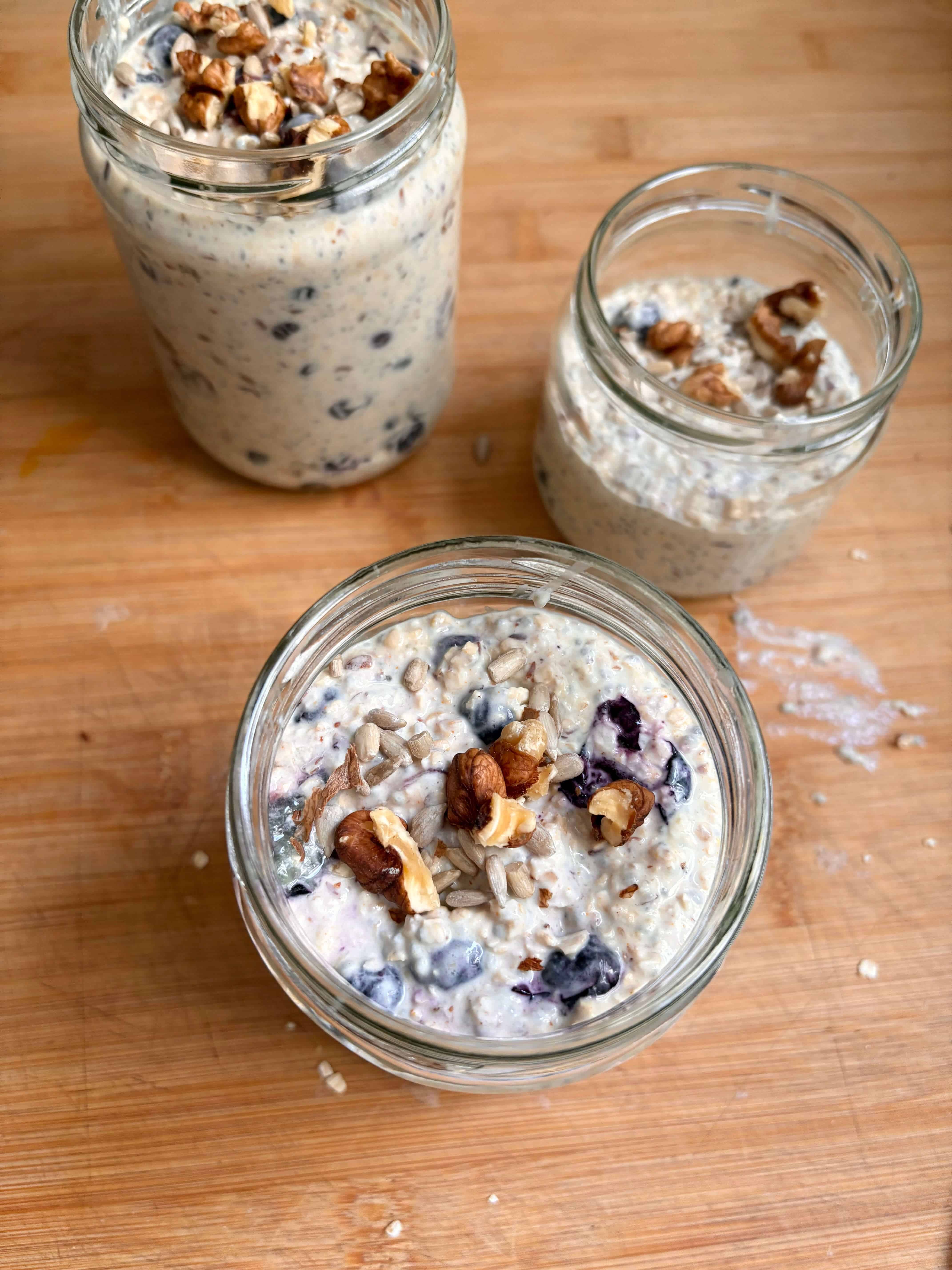 Blueberry overnight oats in glass jars topped with walnuts and sunflower seeds on a wooden surface.
