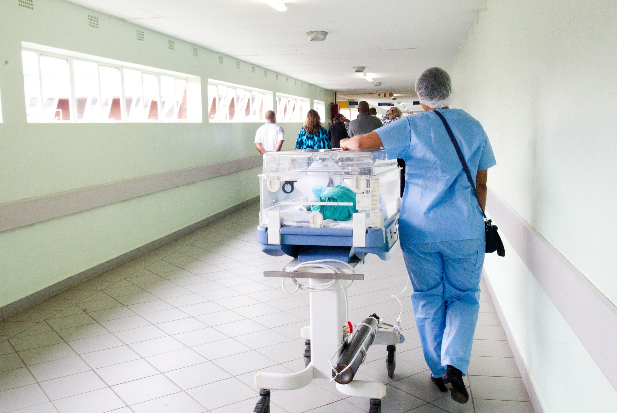 Healthcare worker transporting a neonatal unit in a hospital hallway, representing financial challenges in healthcare related to staffing and equipment costs.