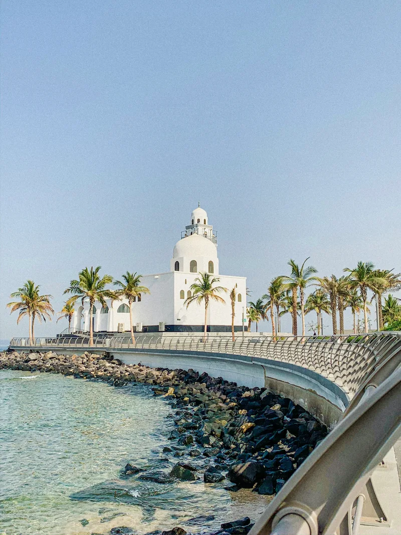 Seaside mosque on the Jeddah Corniche, Saudi Arabia, with palm-lined walkway curving along the Red Sea.