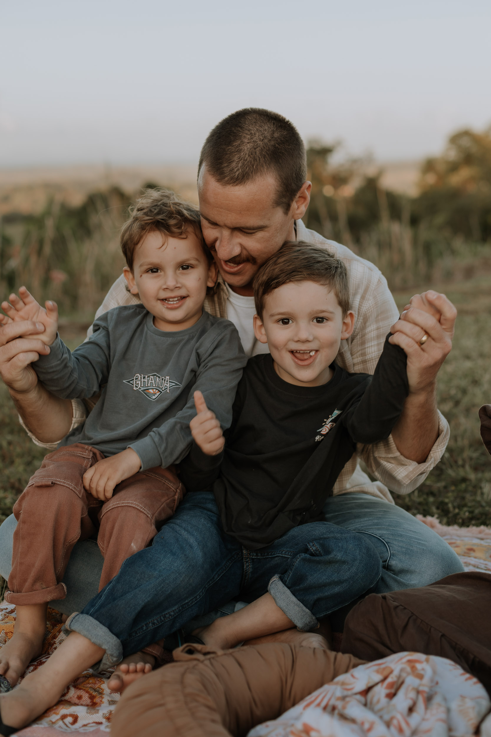 Natural family photography at sunset with parents holding their children and sitting together.