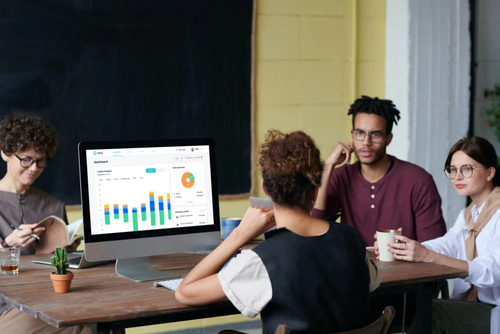 A team sitting aound a table looking at the Net0 dashboard on a computer screen