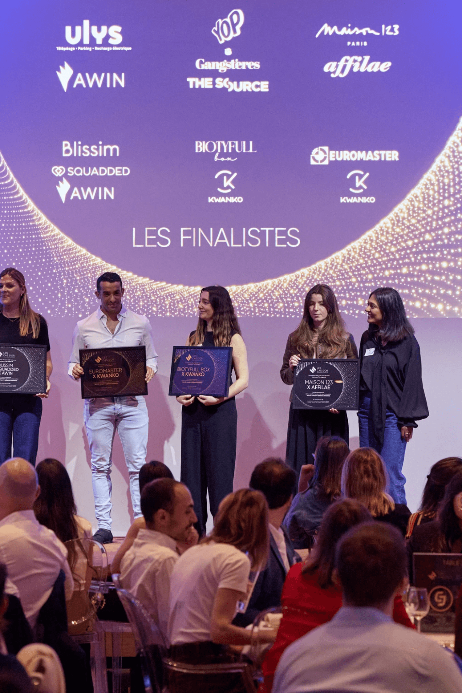 A man in a grey shirt sits in a dim office, gazing seriously at a computer screen. Blinds and office supplies create a focused and professional atmosphere.