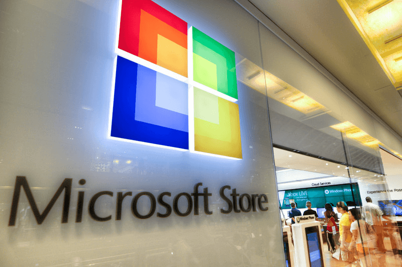 Microsoft Store sign with a bright, colorful logo on a glass wall, with a retail interior visible in the background.