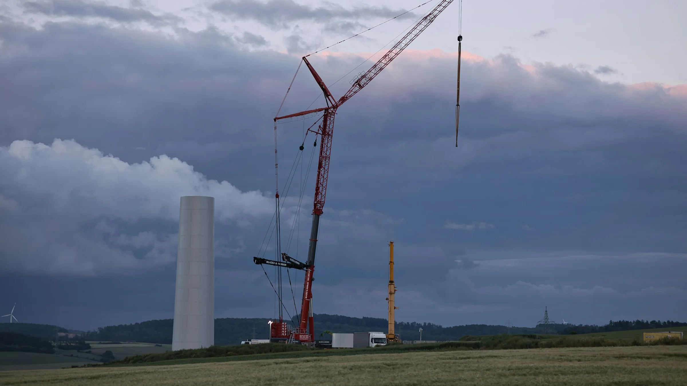 A tall crane lifting a wind turbine component at a construction site in a green field