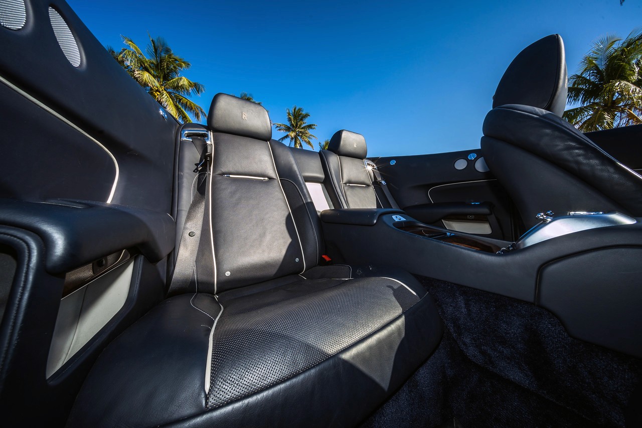 Open door interior shot of the Rolls-Royce Dawn, showcasing the plush black leather seats and high-end detailing.