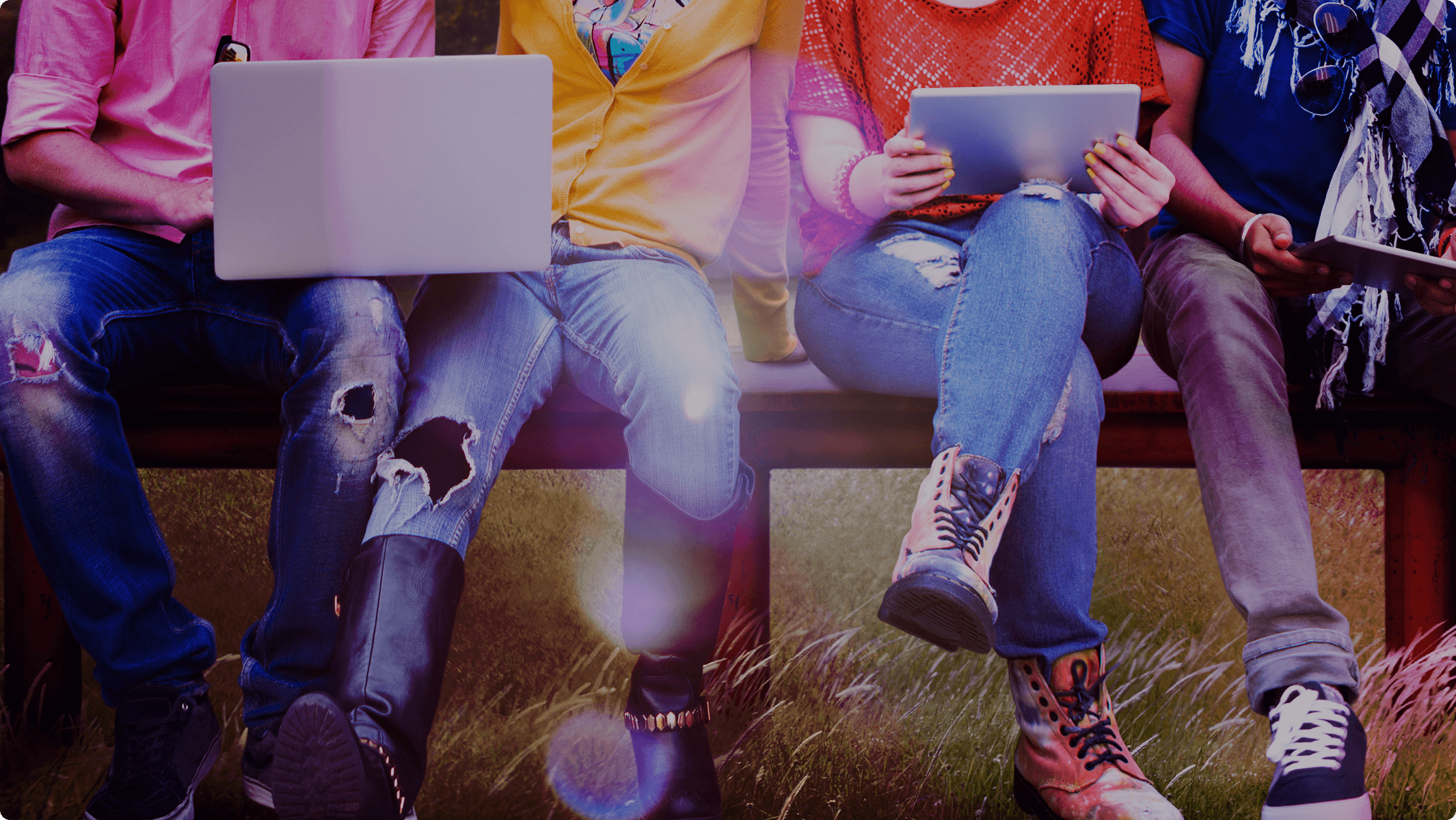 Neck down shot of a group of people on a bench holding laptops and tablets