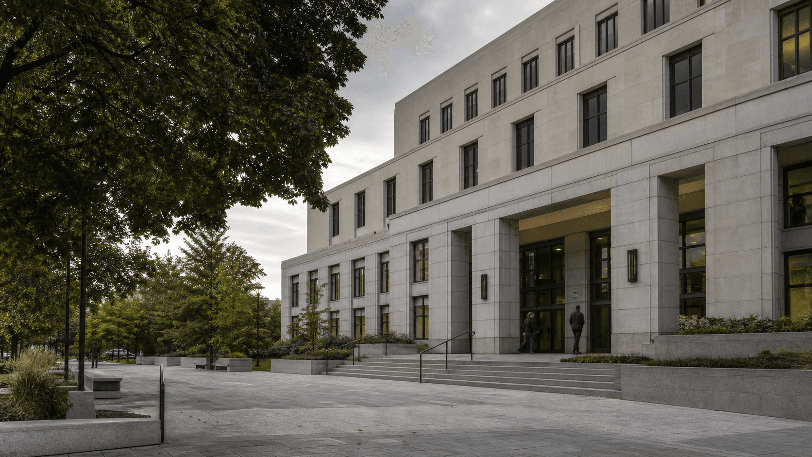 A civic administration building with a stone facade and landscaped public forecourt.
