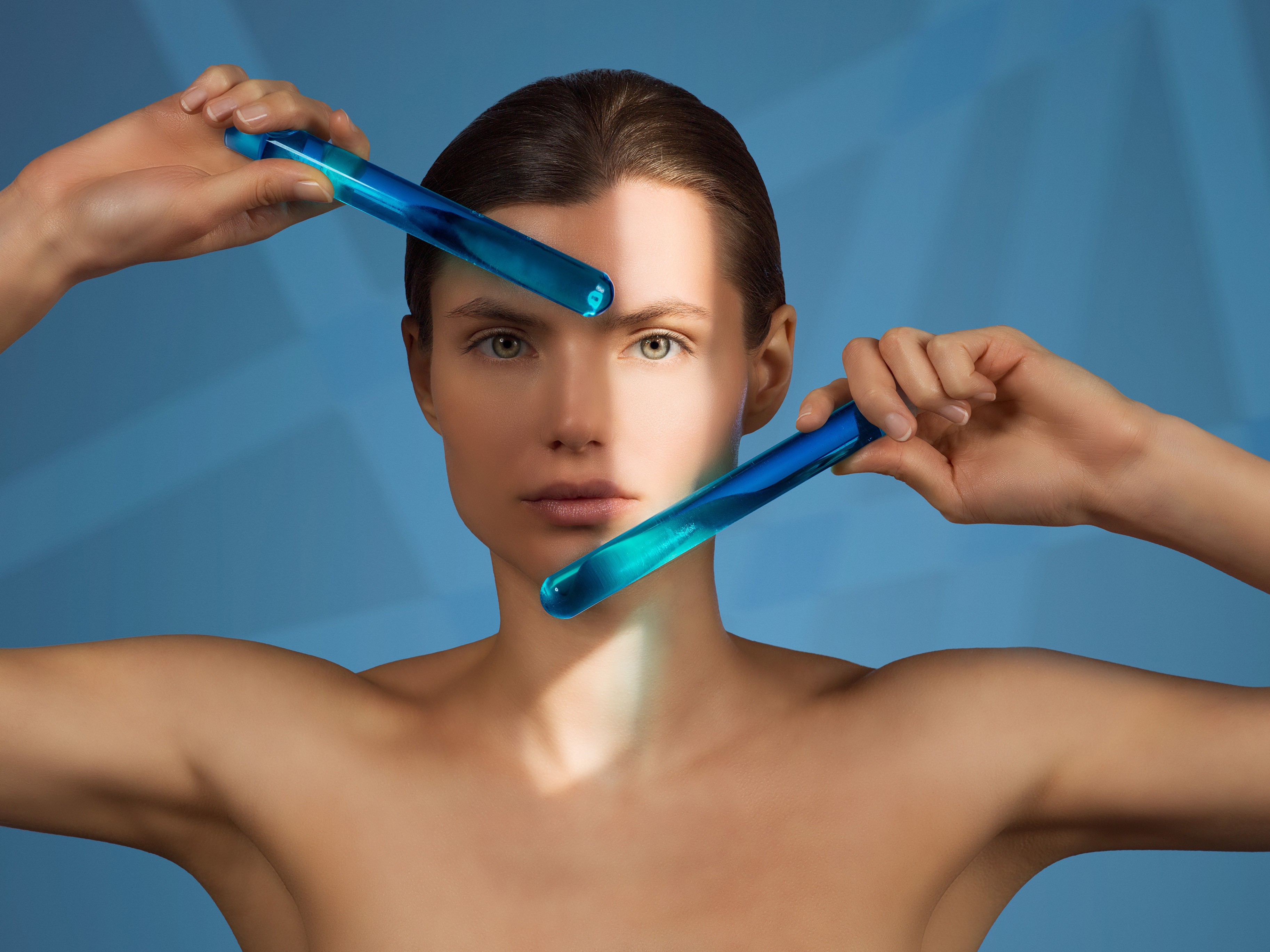 Model holding blue glass rods across face in artistic shoot for Saypha hyaluronic acid dermal fillers