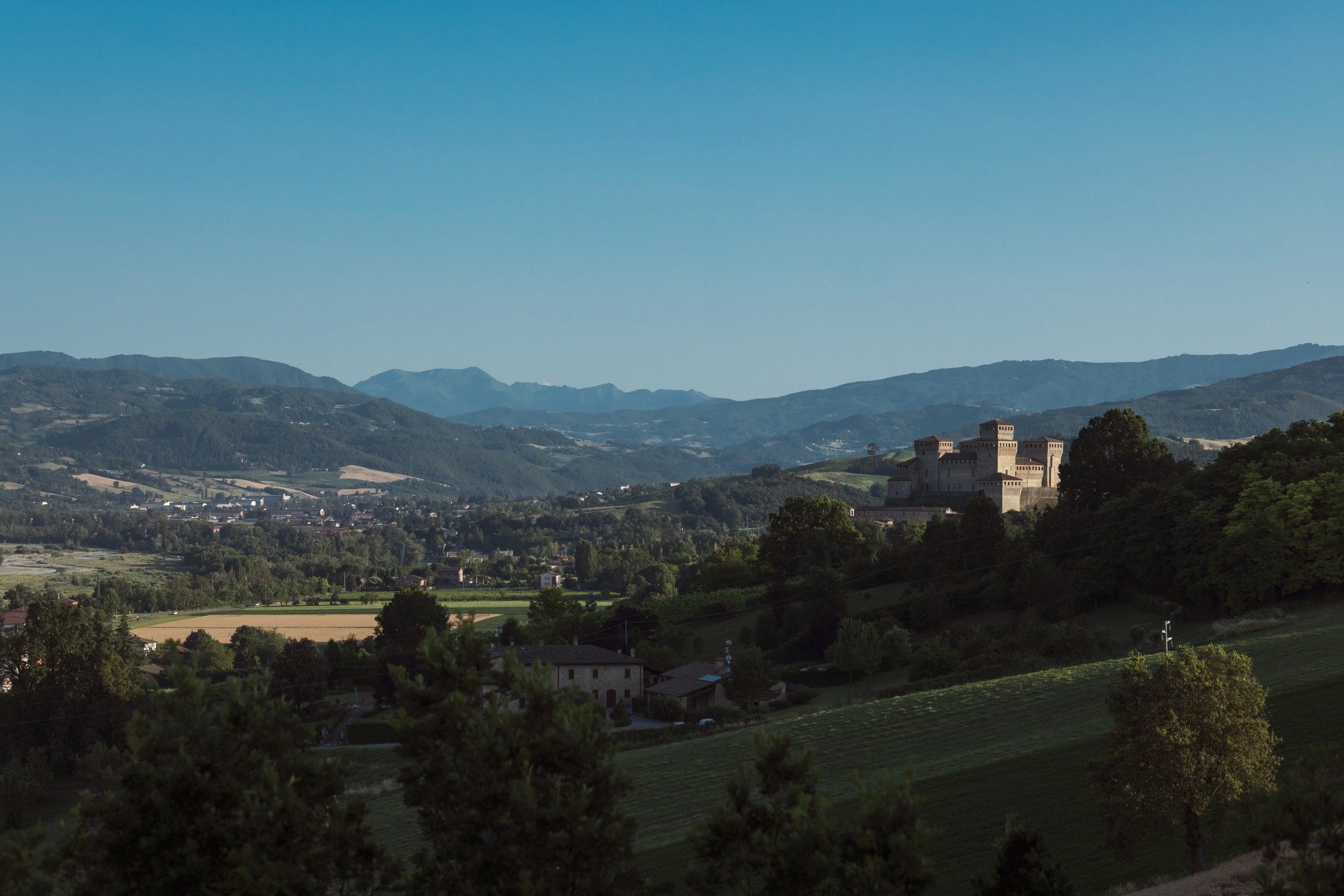 Paesaggio collinare con castello medievale sullo sfondo, campi verdi e cielo terso in Toscana