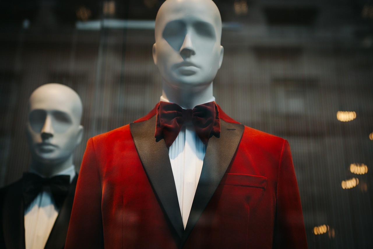 Mannequin wearing a red velvet tuxedo jacket with black lapels and a bow tie, displayed in a storefront window.