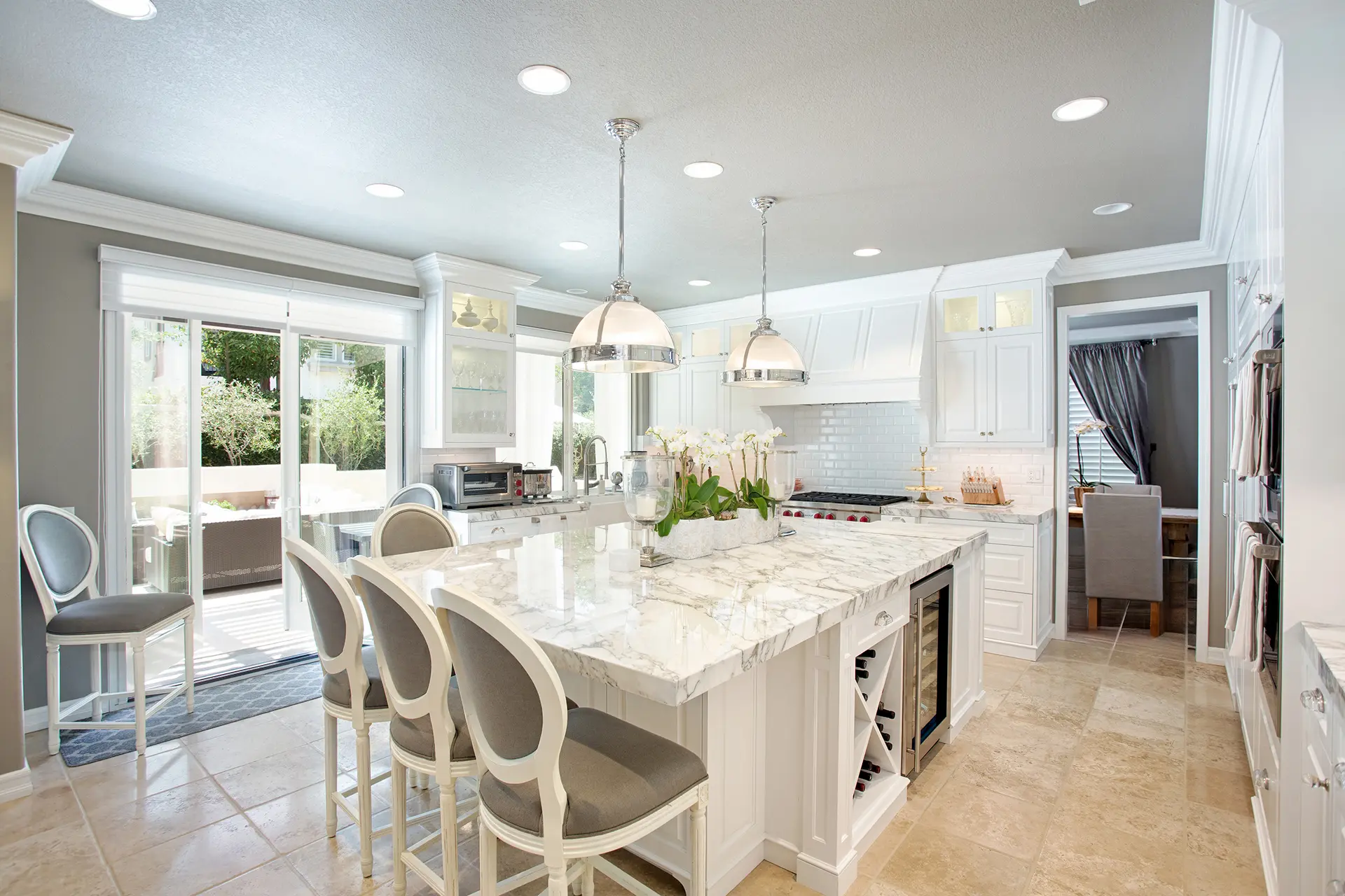 'Newport Beach Remodel' kitchen with marble island, white cabinetry, and pendant lighting, opening to a patio.
