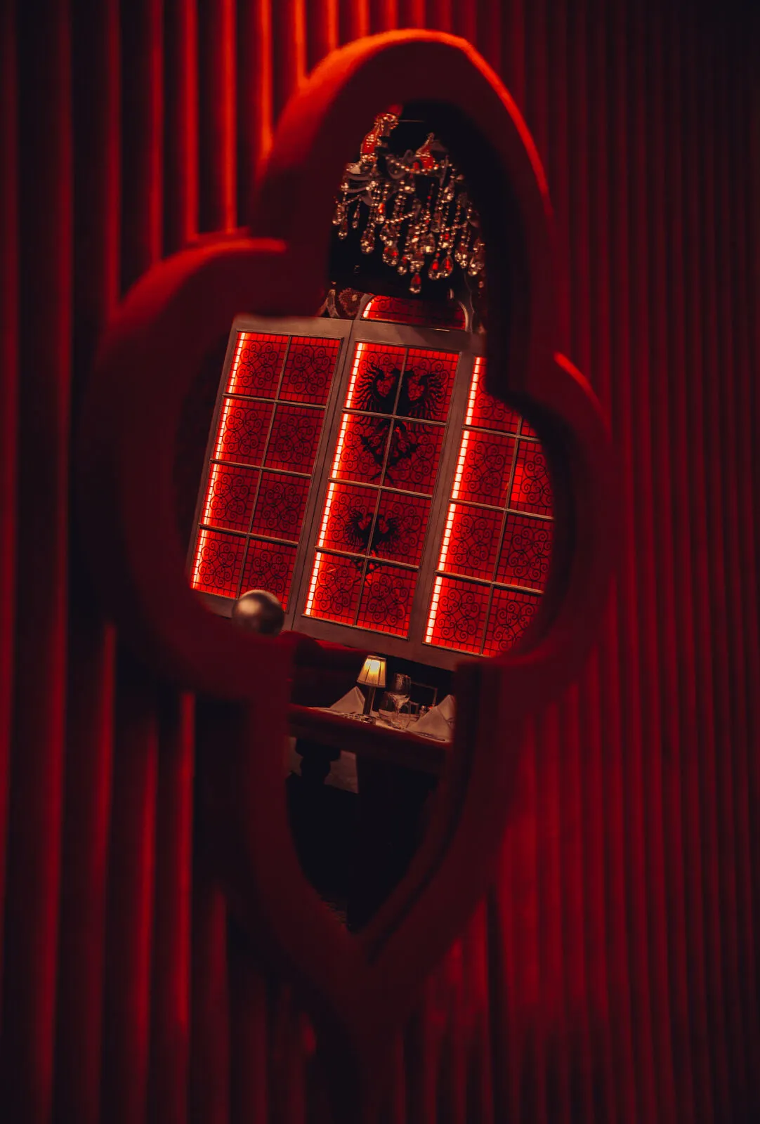 Red-lit stained glass panels with double-headed eagles and a crystal chandelier, reflected in a velvet-framed mirror at Raspoutine Dubai