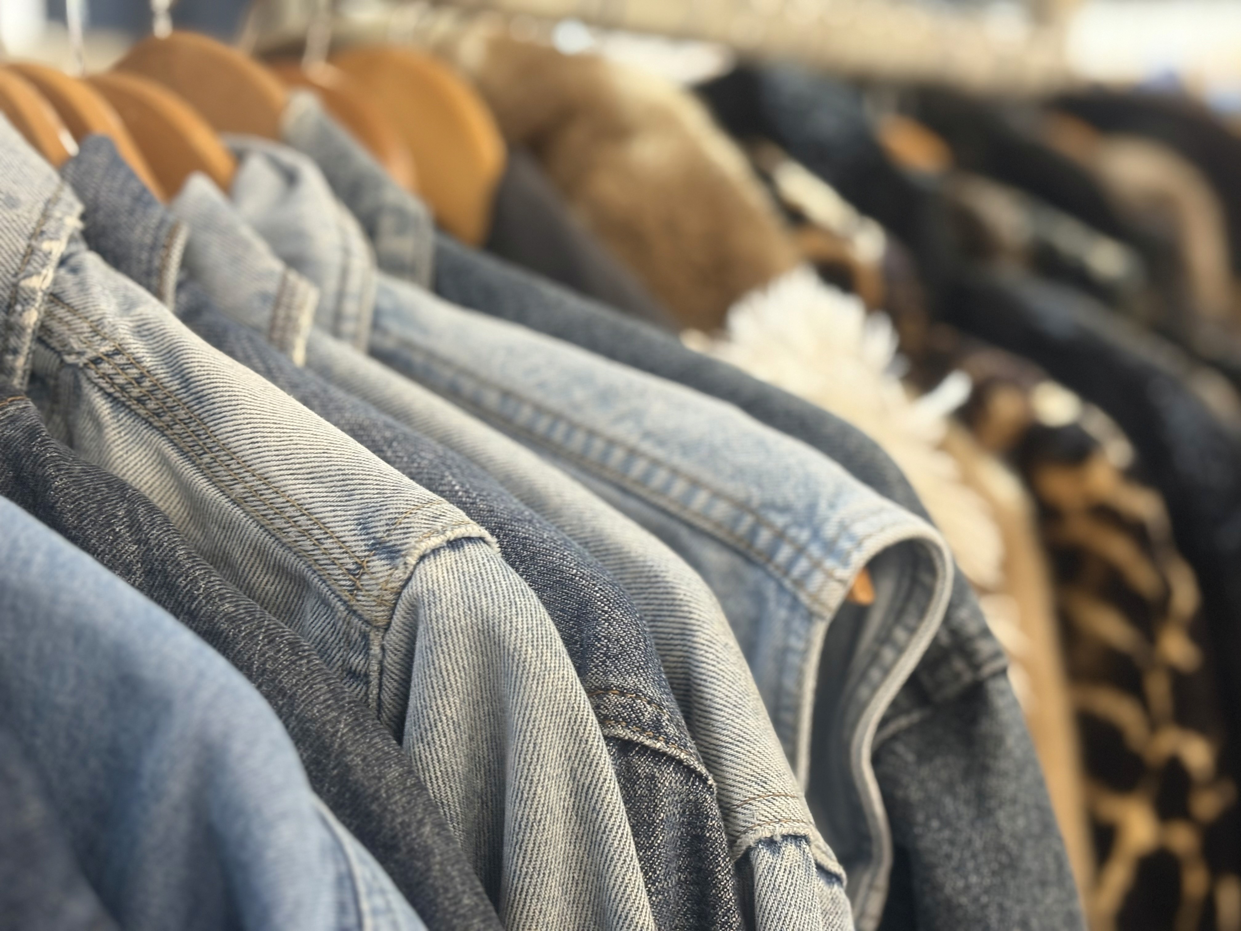 Rack of denim jackets and fur coats on wooden hangers, close-up.