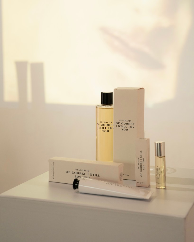 A collection of beauty products displayed on a white surface, including a bottle of fragrance, a box, and a small tube.