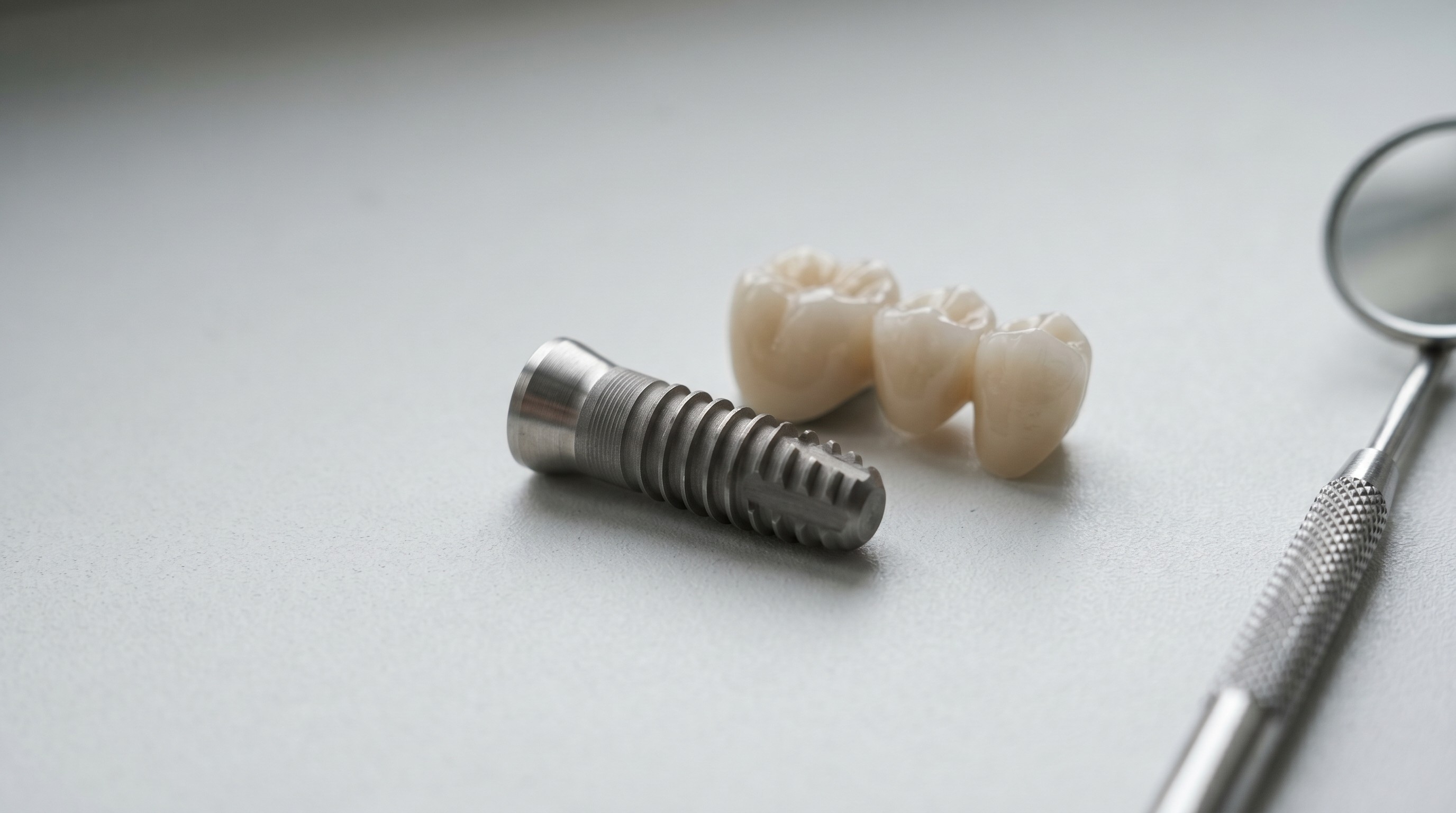 Titanium dental implant model beside a three-unit porcelain bridge on a clinical surface