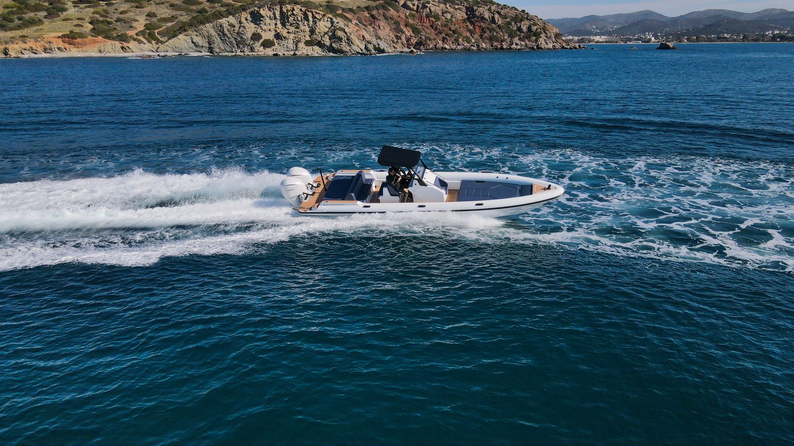 White Rock 36 speedboat with captain at helm cruising calm blue waters near Paros coastline with hills in background.