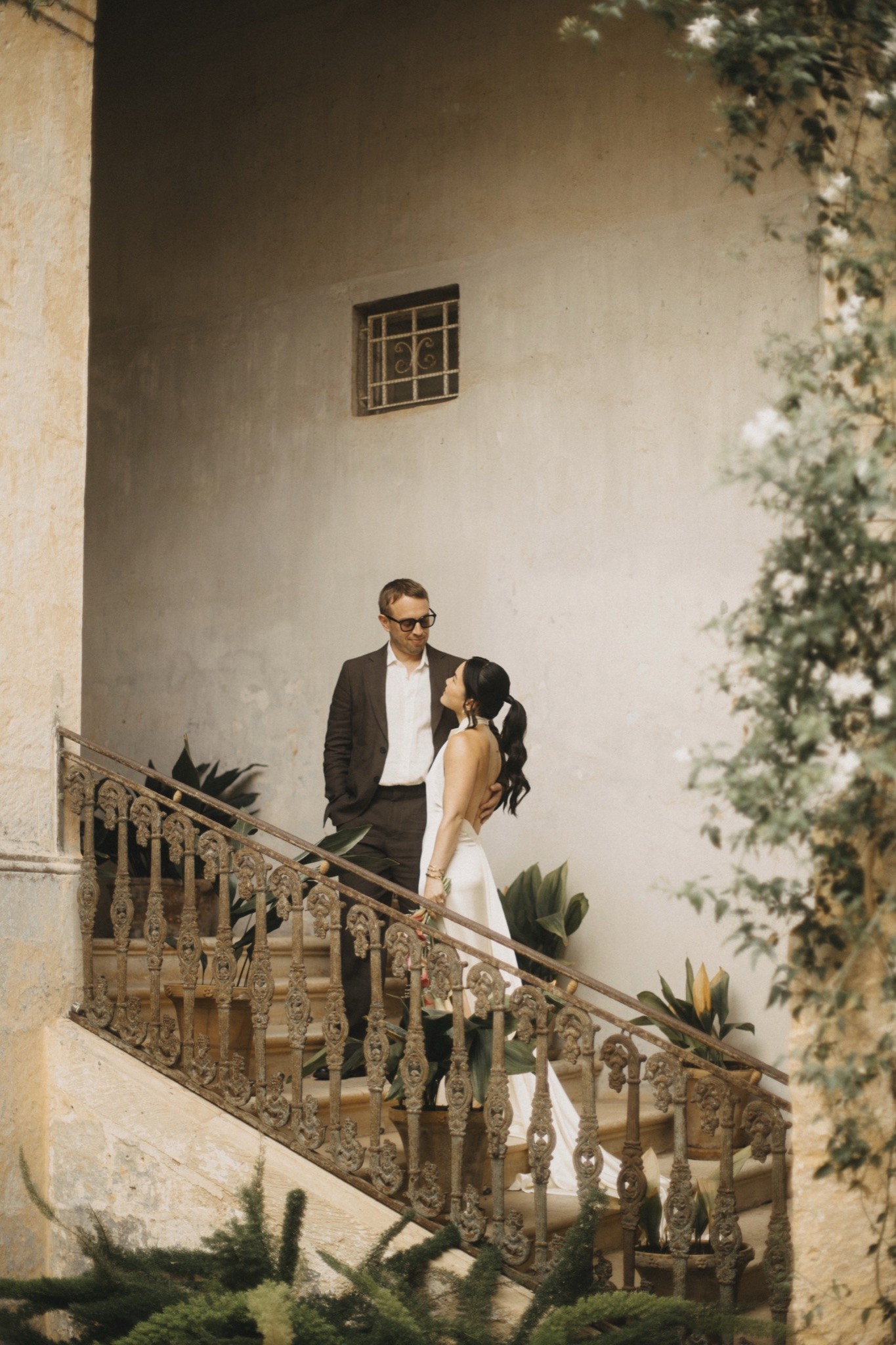 Toey and Otto sharing a look on an old stone staircase draped in jasmine