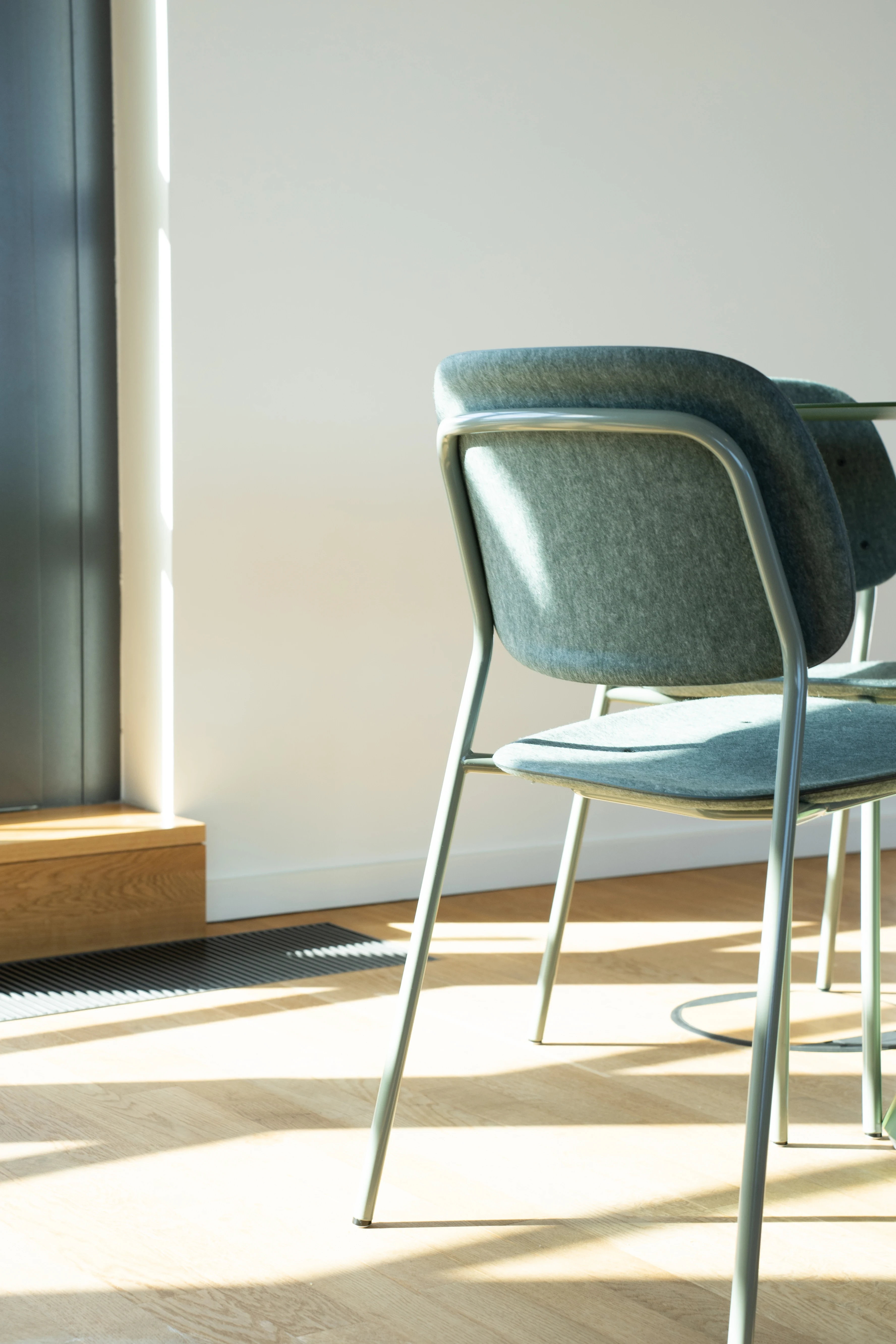 Close-up of sage-green chairs with felt upholstery and tubular frames at AI START-UP MUNICH, lit by warm sunlight on oak flooring.