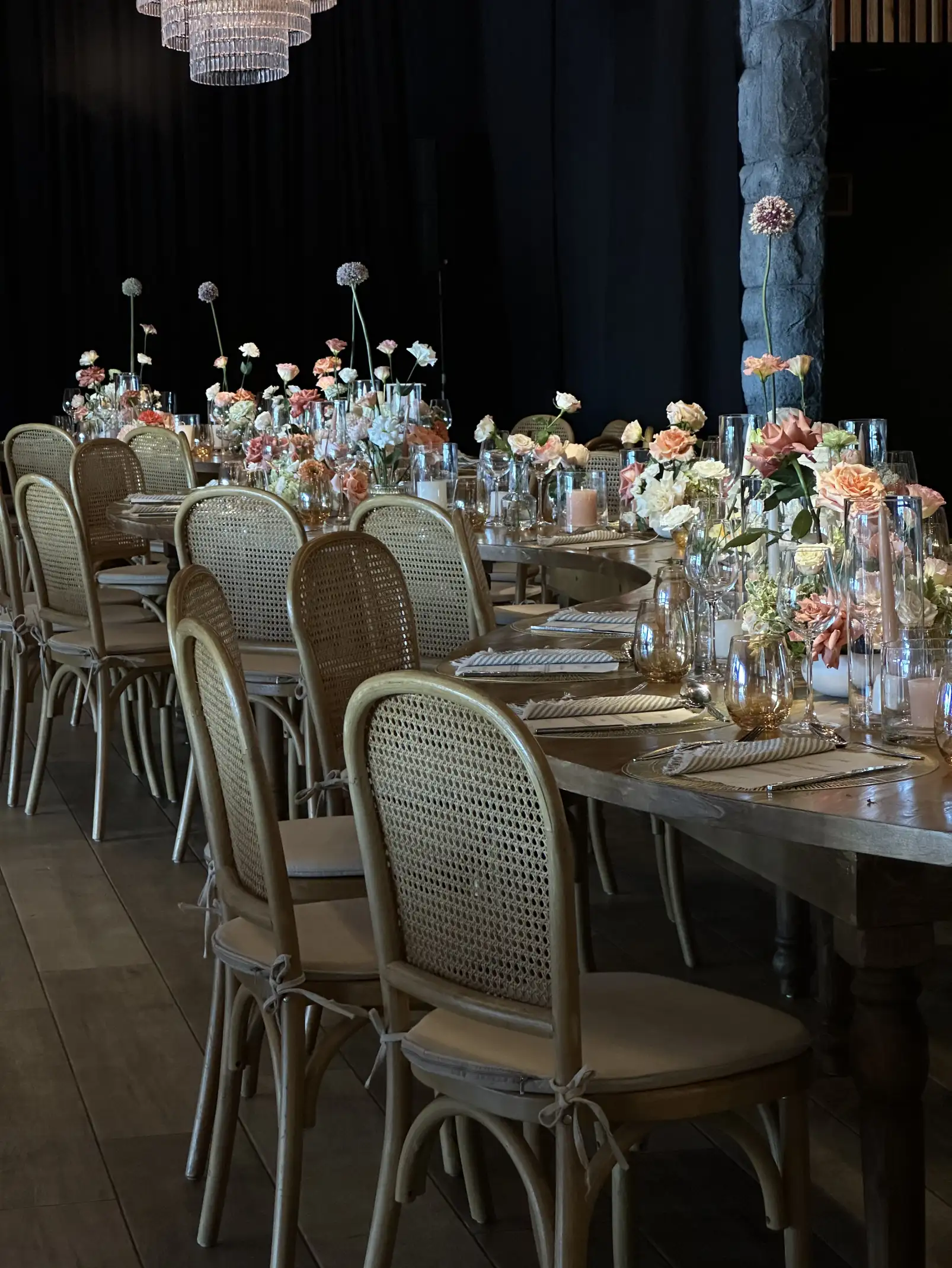 Mesas largas con sillas de ratán y arreglos florales elegantes en tonos suaves, bajo una iluminación cálida.