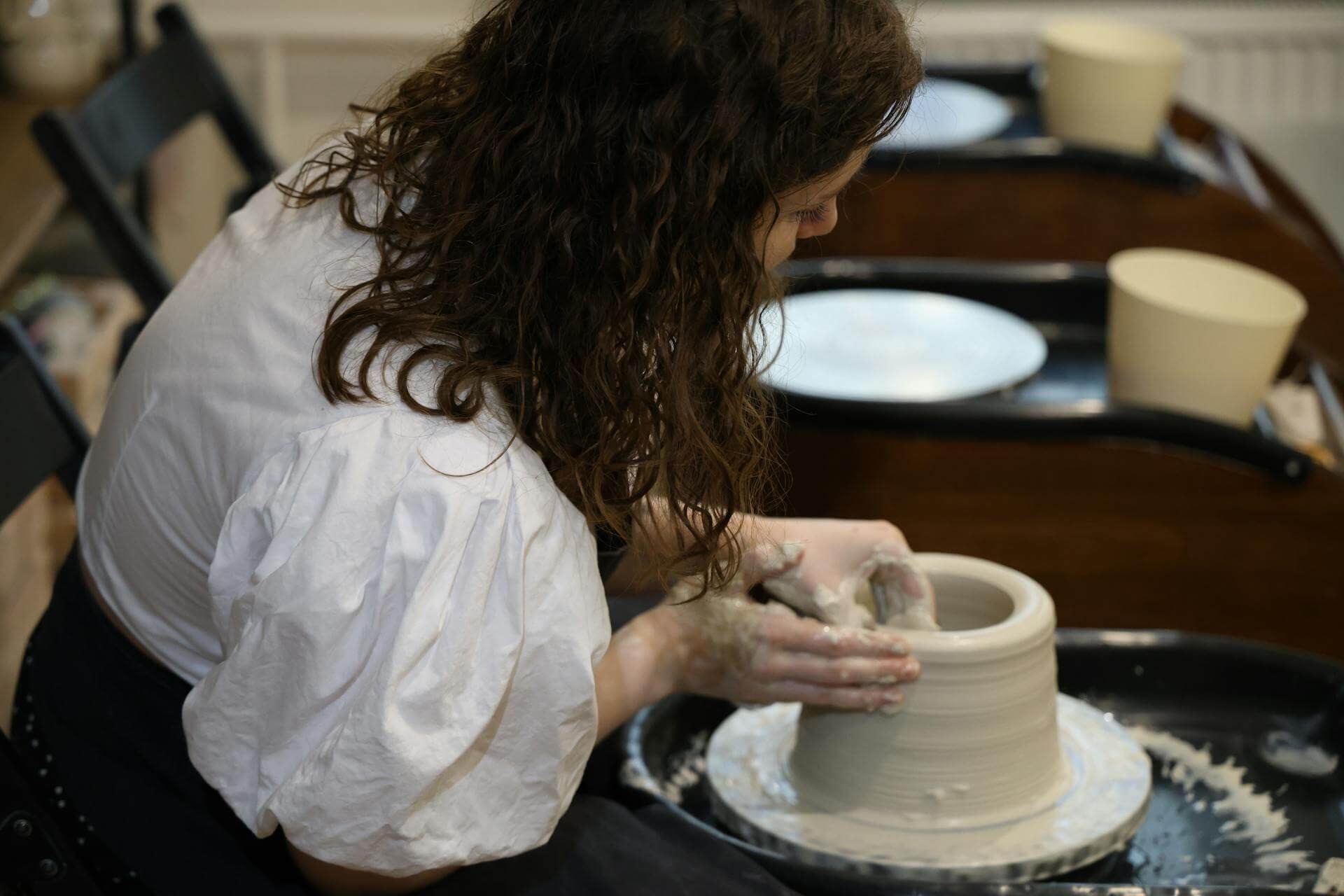 A woman skillfully shapes clay into a pot on a spinning potter's wheel in a serene workshop setting