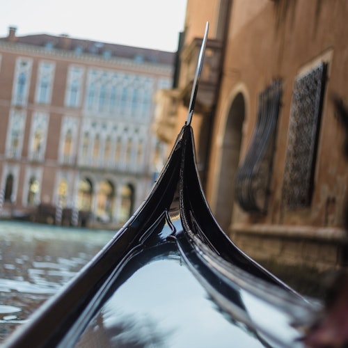 Close-up of a gondola's prow against a canal with historic buildings and water in the background in Venice, Italy.