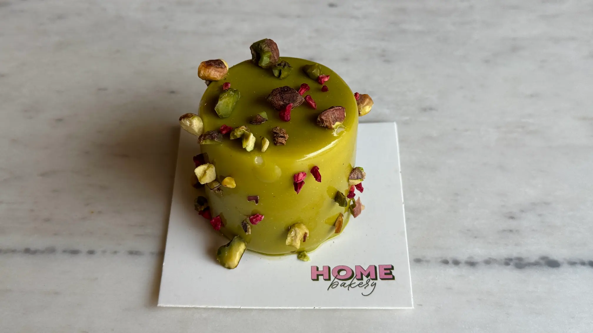 Pistachio mousse cake with green glaze, decorated with pistachios and rose petals