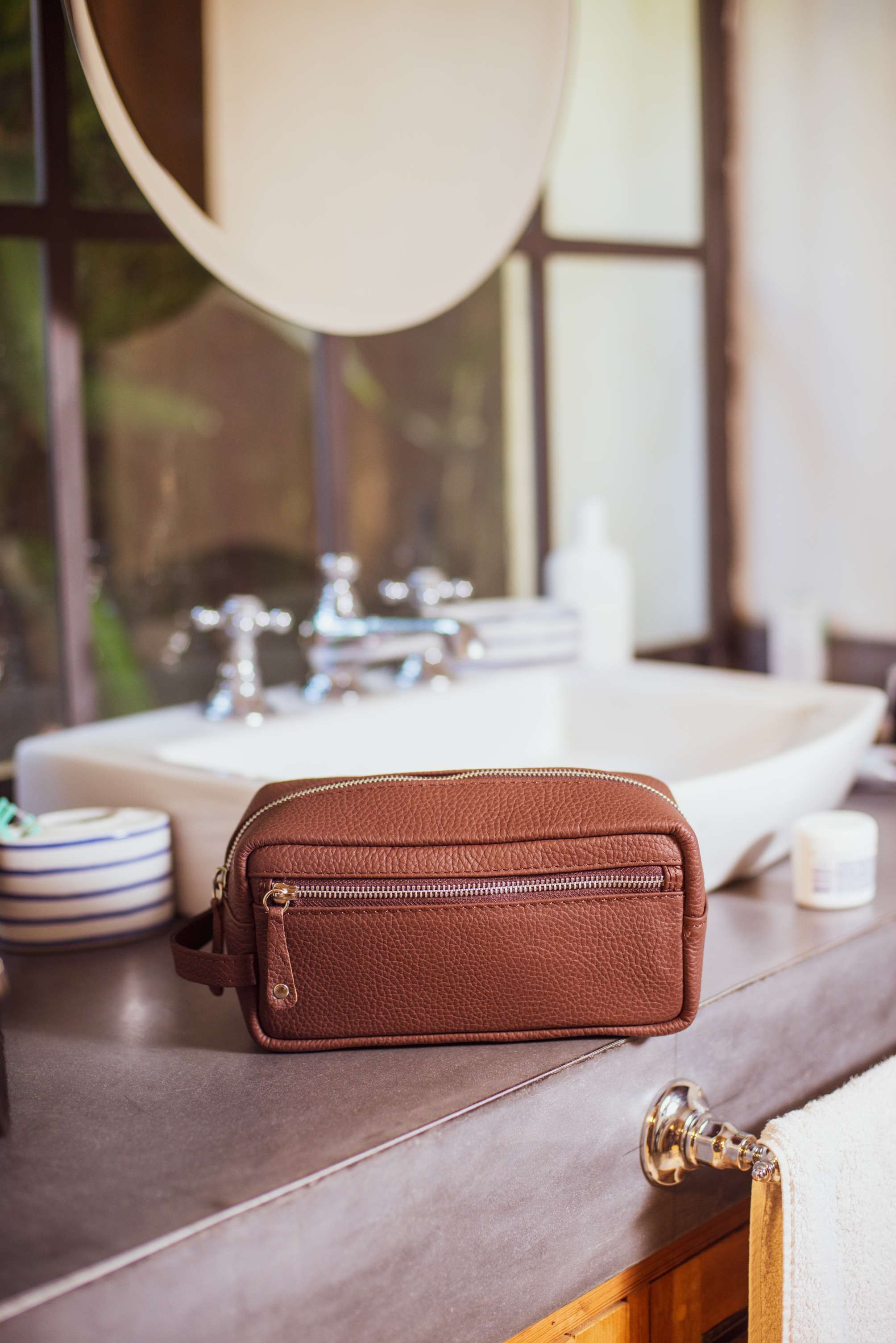 A smiling woman with her arms crossed, standing against a dark green background. She has long, dark hair.