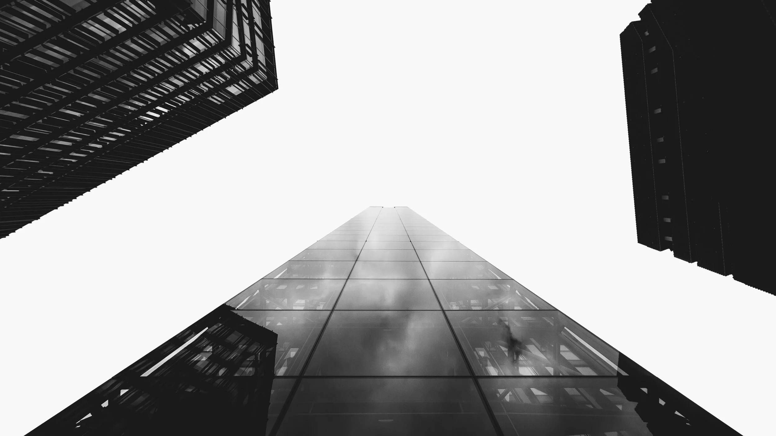 :A black and white abstract image showing a view upward between two tall buildings towards a light source.