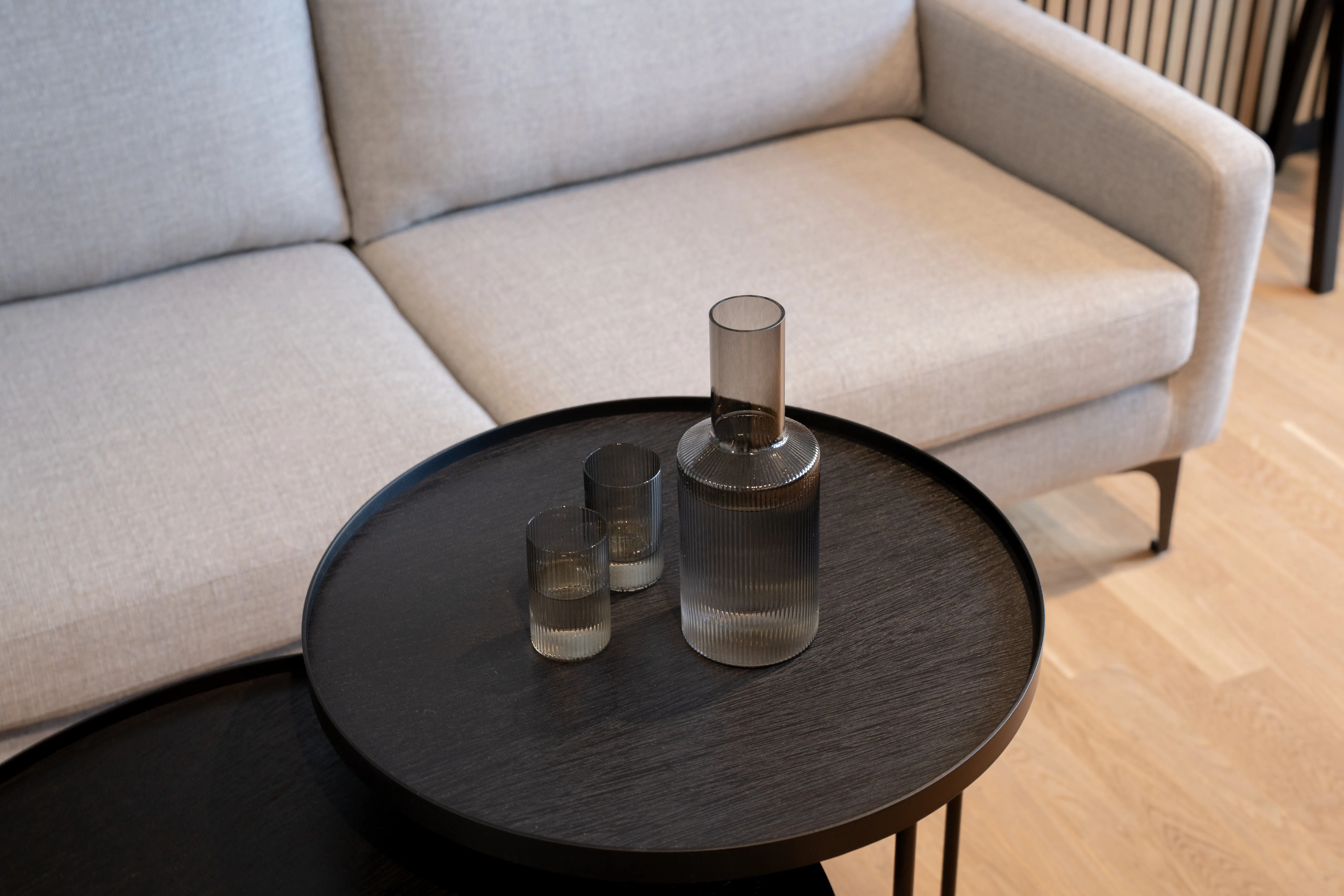 Detail of a black round tray table with a ribbed glass carafe and two glasses in front of a light grey sofa at AI START-UP MUNICH.