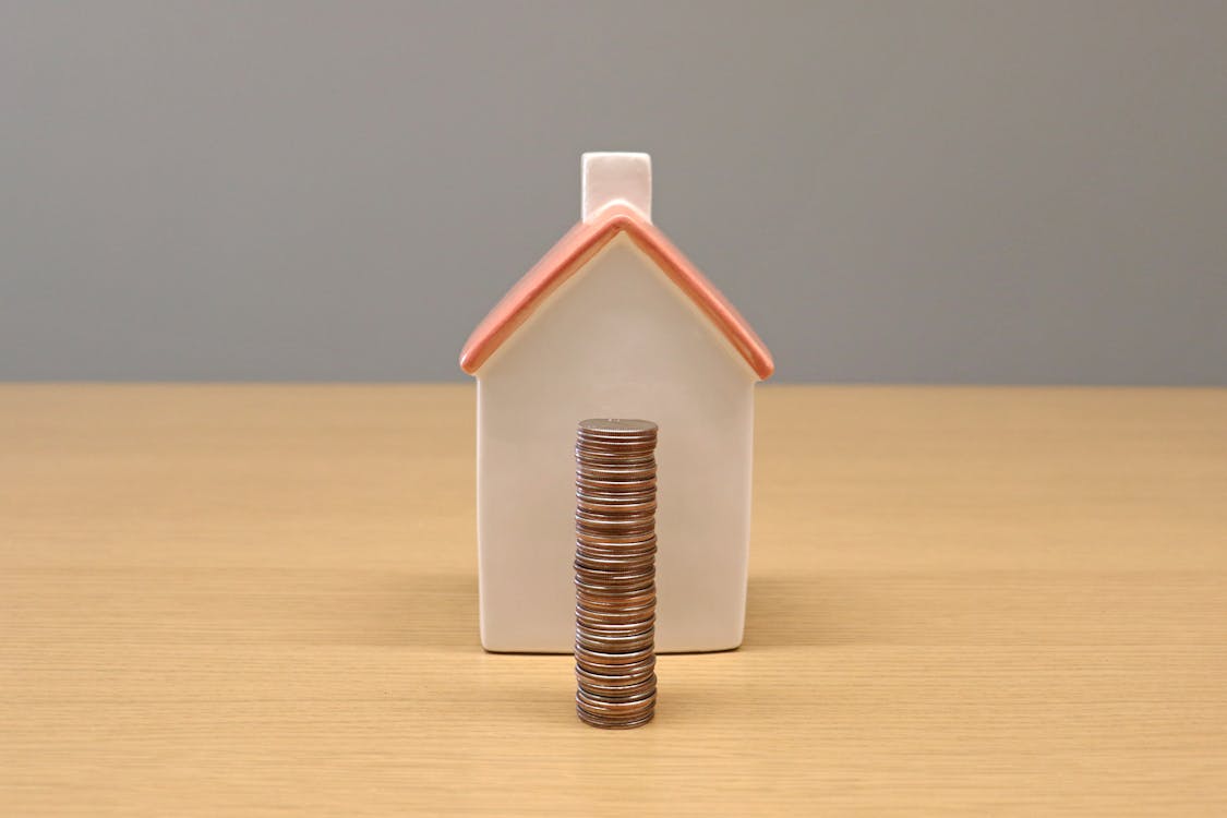 Free A conceptual still life image of stacked coins in front of a porcelain house, symbolizing savings and investment. Stock Photo