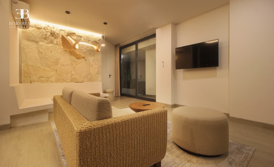 Cozy woven sofa and stone feature wall in the living room of the three bathroom Echo Beach Suite apartment, Bali, Canggu, with patio access.