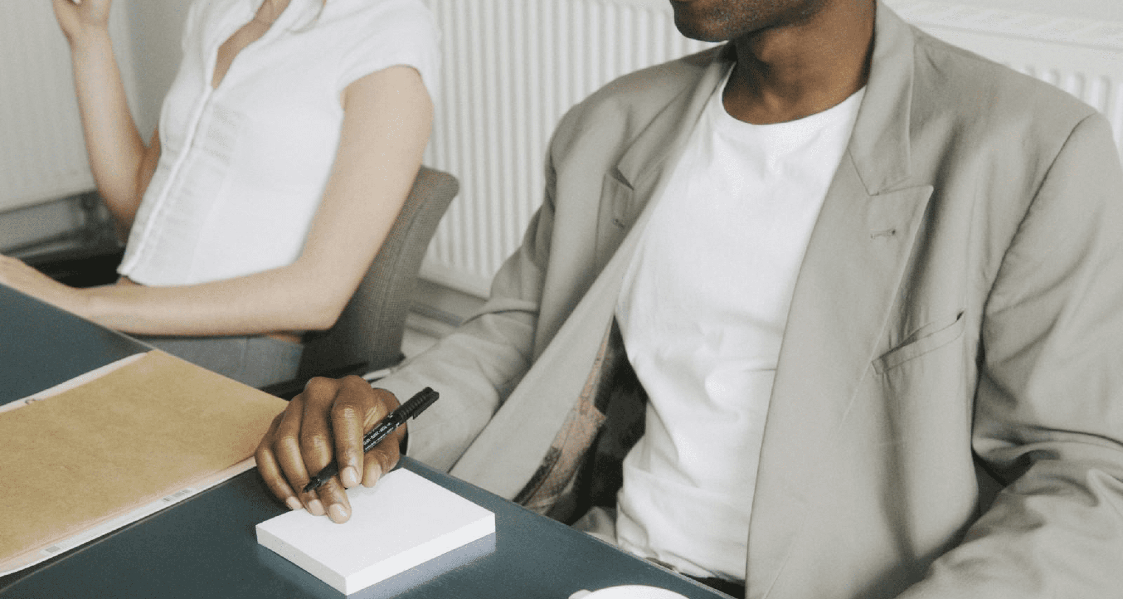 A man and woman sit at a table, focused on a notepad, engaged in discussion or brainstorming ideas together.