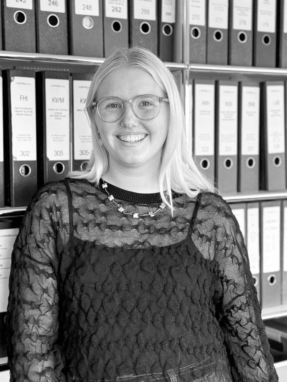 Porträt von Emma Rehsing, Werkstudentin und Bauzeichnerin bei Beinker Architektur, vor einem Regal mit Aktenordnern im Büro.