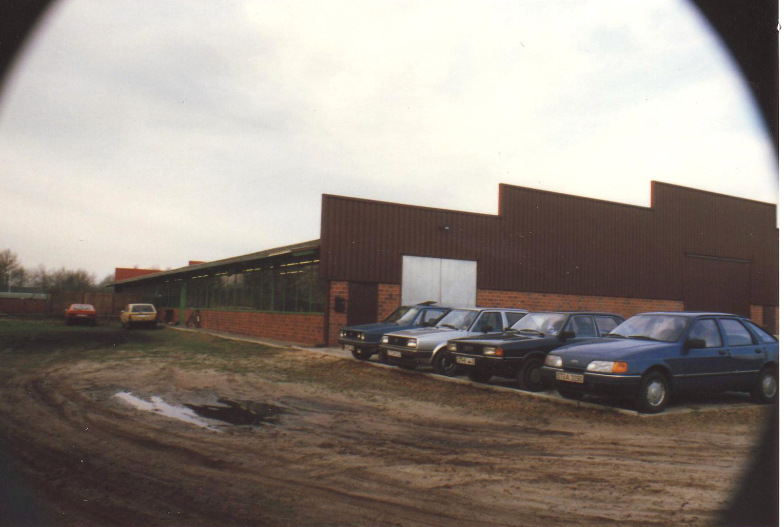 Industriegebäude mit Parkplatz und Autos. Roter Backsteinbau, Zickzack-Dach. Gewerbegebiet.