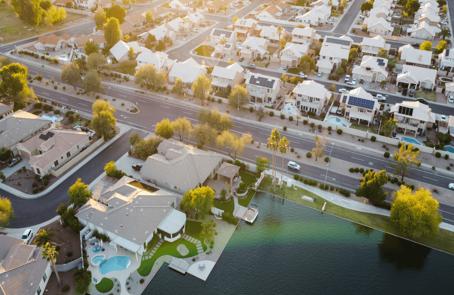 Aerial view of a suburban neighborhood with houses, roads, and a lake, captured during the daytime.