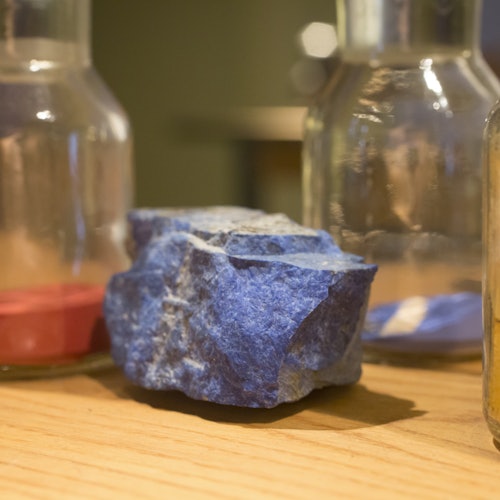 A rough blue stone placed on a wooden surface surrounded by three clear glass bottles.