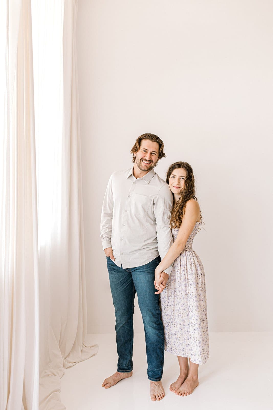 A couple standing together holding hands, barefoot, in front of a large window at Revelator Studio in Shreveport.