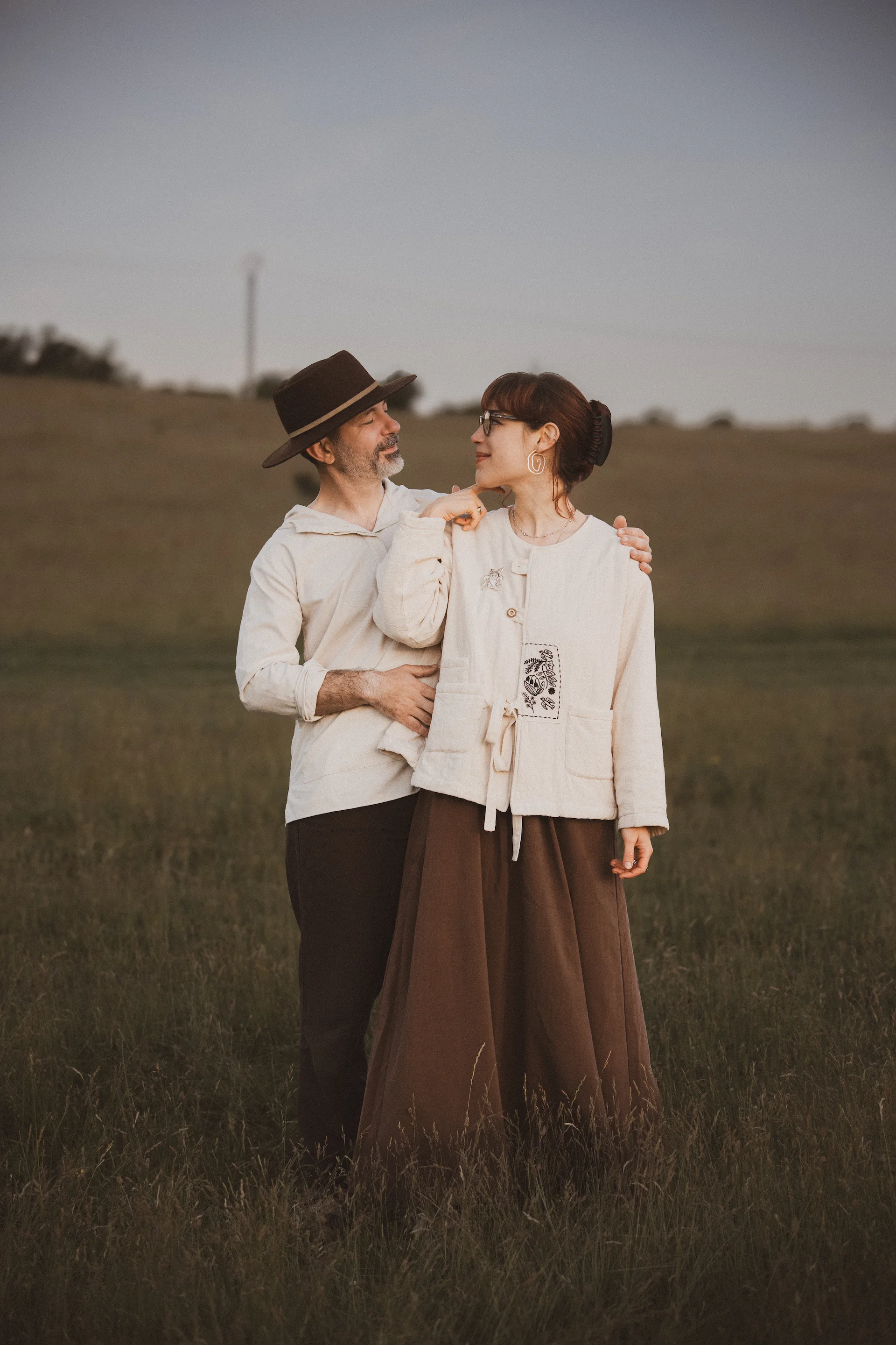 Cosmin și Ioana zâmbind unul la celălalt, îmbrăcați în haine luminoase pe un fundal de câmp